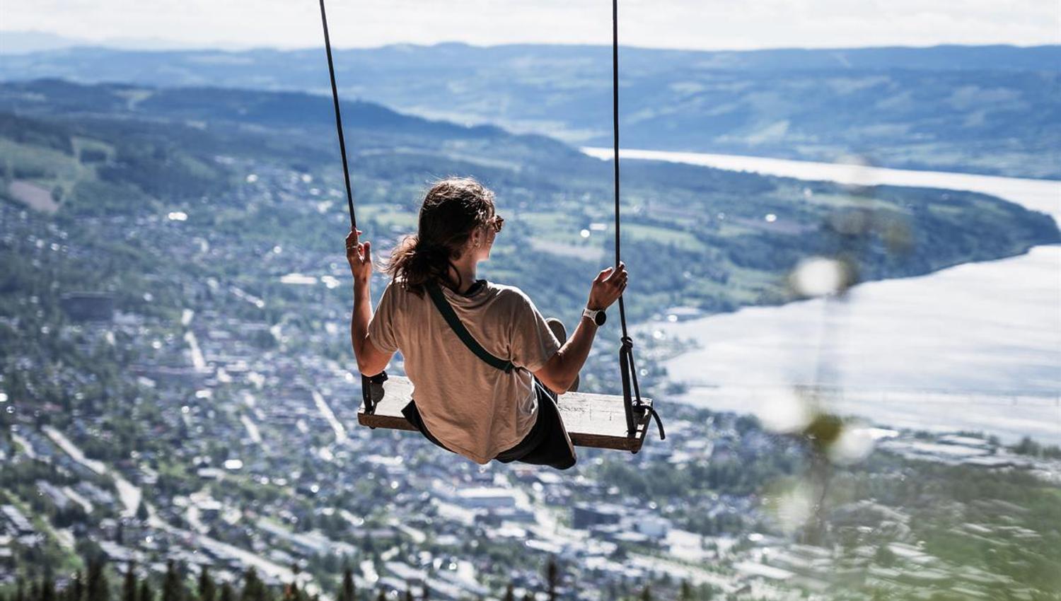 Person on a swing overlooking a town and lake.