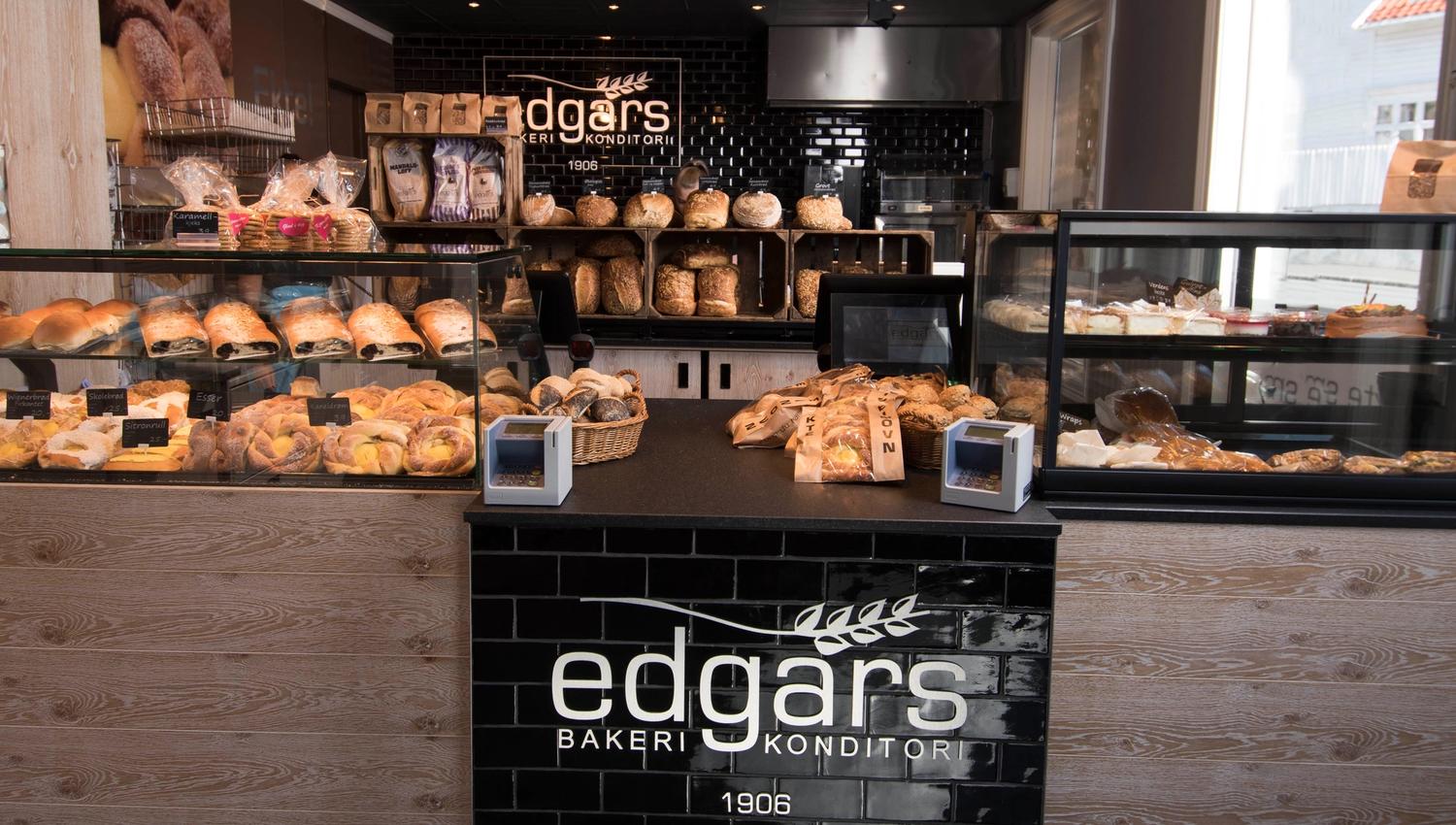 Inside the bakery, by the counter. Lots of delicious pastries and slices of cake on each side of the counter.