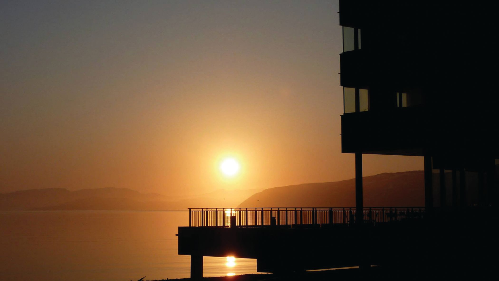 Silhouette of a building by a lake at sunset, with warm golden hues reflecting on the water.
