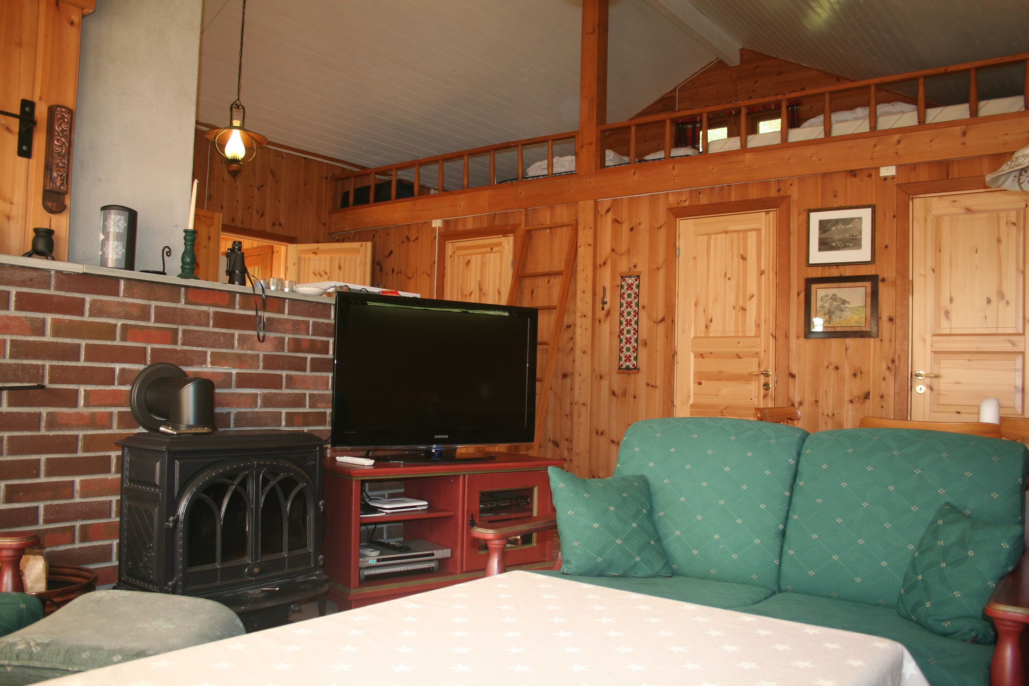 Traditional Norwegian cabin living – living room with a wood stove, green sofa, and wooden beams.