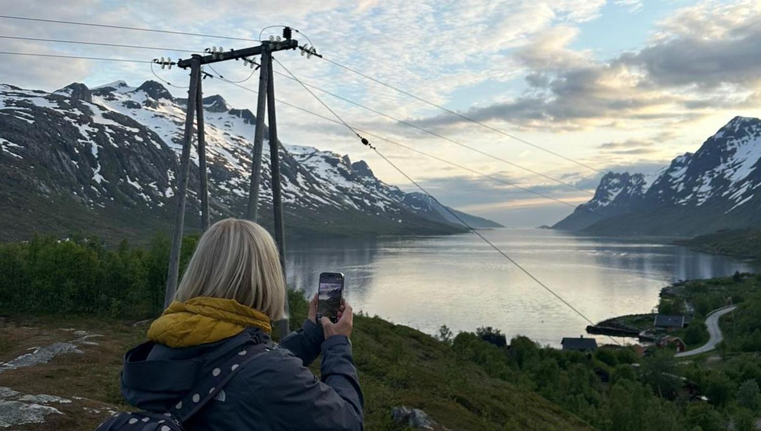 A person taking a picture of the fjord and mountains