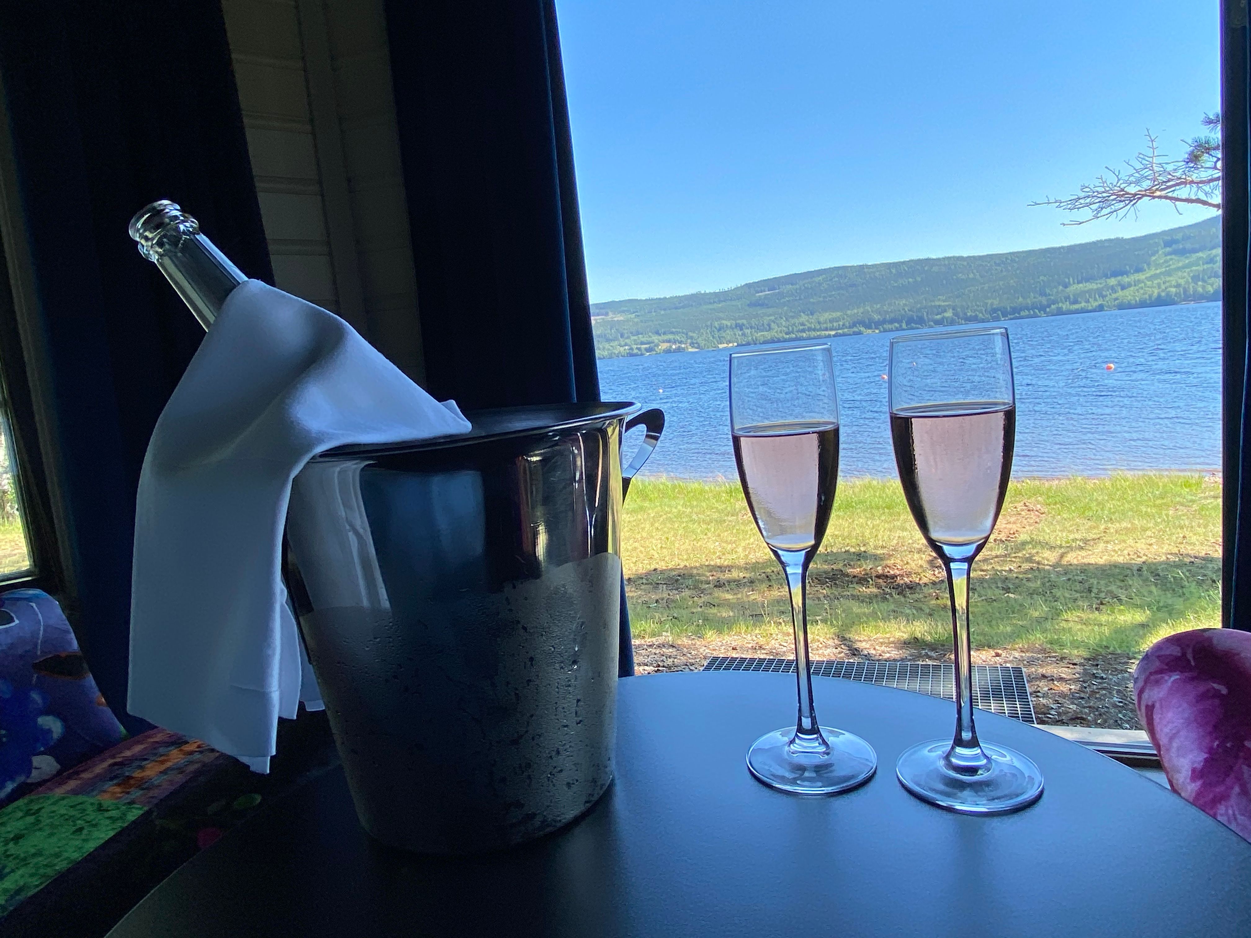 2 glasses with pink drinks on a table with view to a lake 