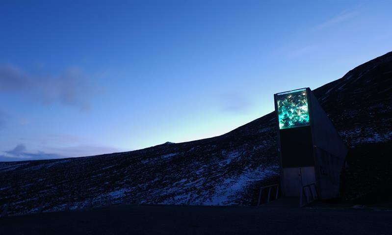 Inngangspartiet til Svalbard Globale Frøhvelv i et mørkt lett snødekt landskap med en klar blå kveldshimmel i bakgrunnen