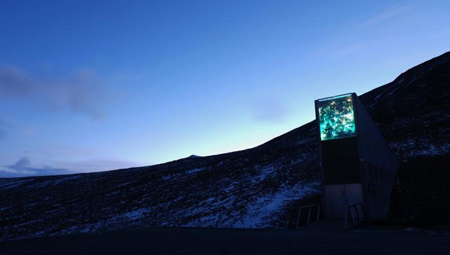 Inngangspartiet til Svalbard Globale Frøhvelv i et mørkt lett snødekt landskap med en klar blå kveldshimmel i bakgrunnen
