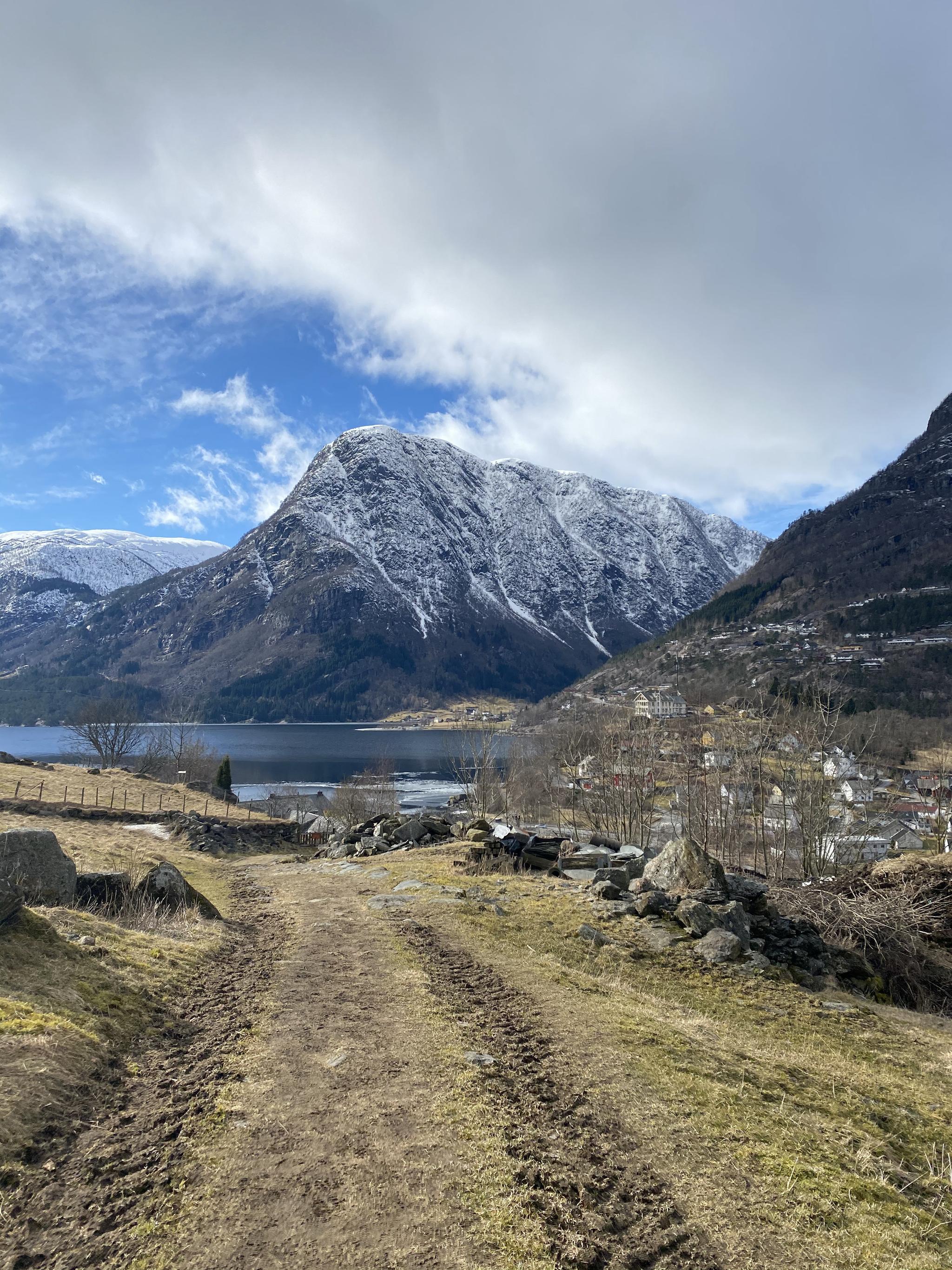 View from the Hjøllo–Mannsåker cultural trail overlooking the Hardanger fjord landscape with snow-covered mountains and blue sky.
