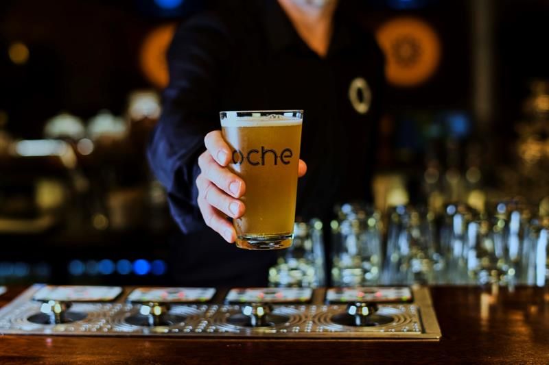 Detalj av hånd som holder et ølglass med Oche-logo på