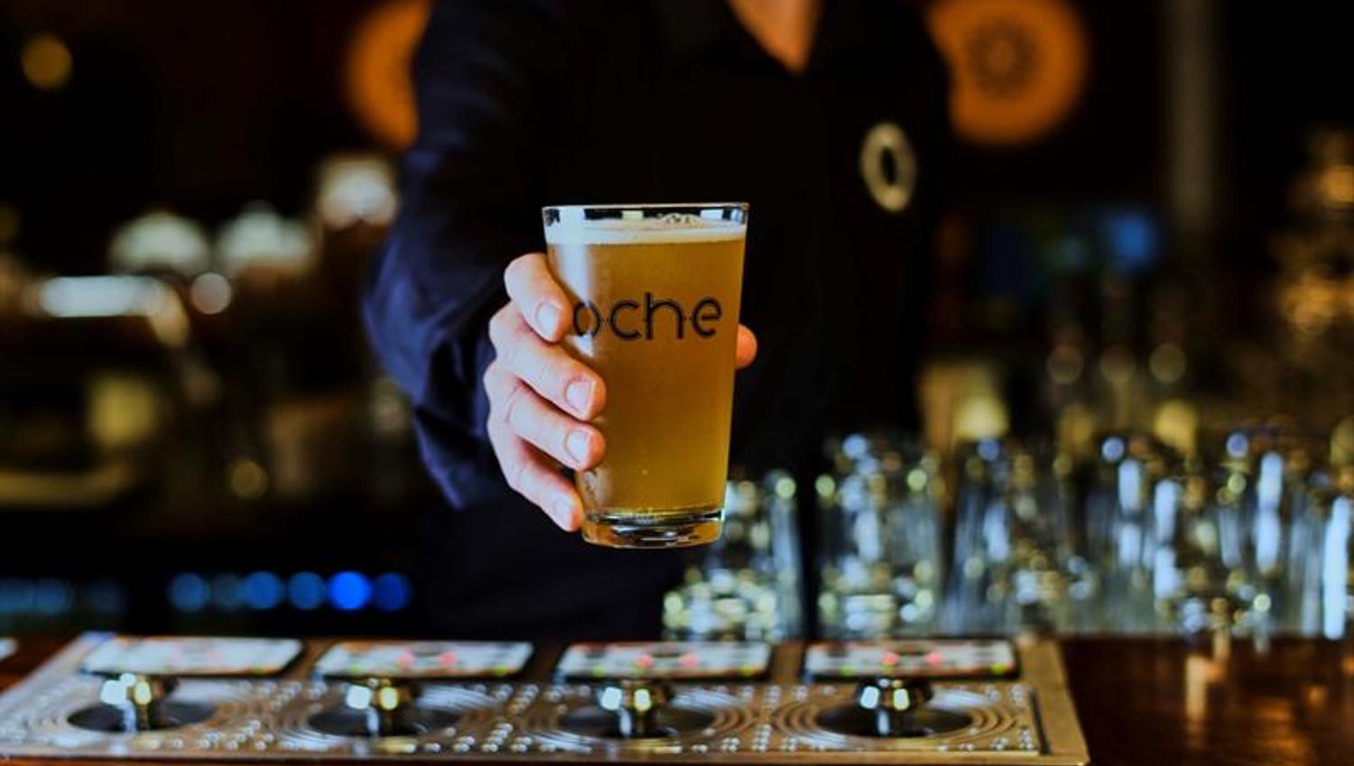 Detalj av hånd som holder et ølglass med Oche-logo på