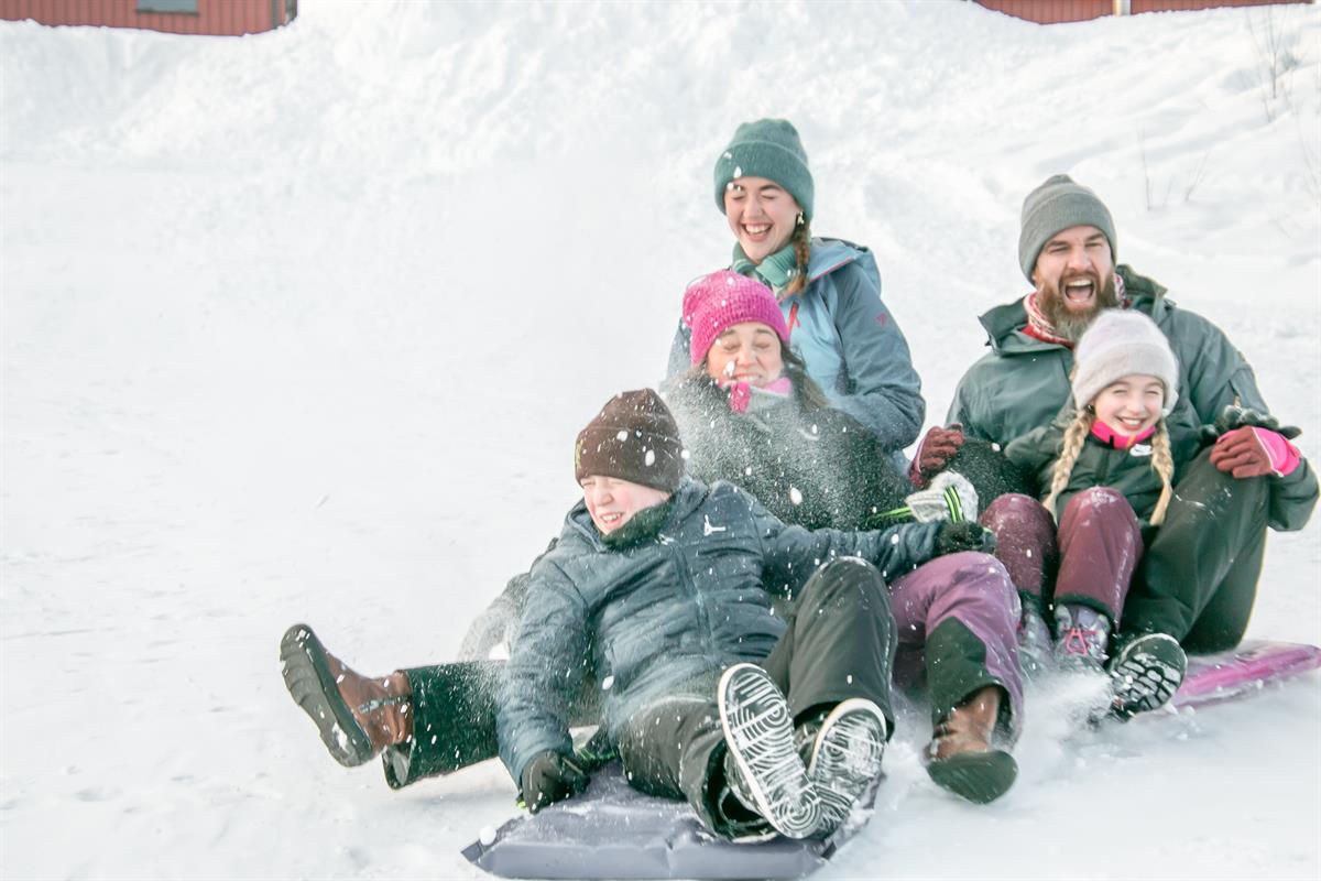 Familie sitter sammen i snøen og smiler mens de tar en vinterpause.