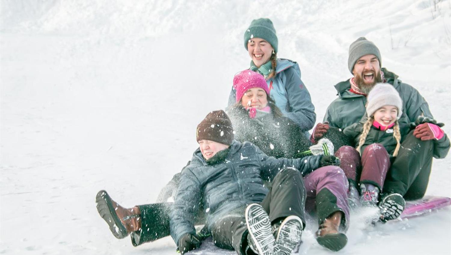 Familie sitter sammen i snøen og smiler mens de tar en vinterpause.