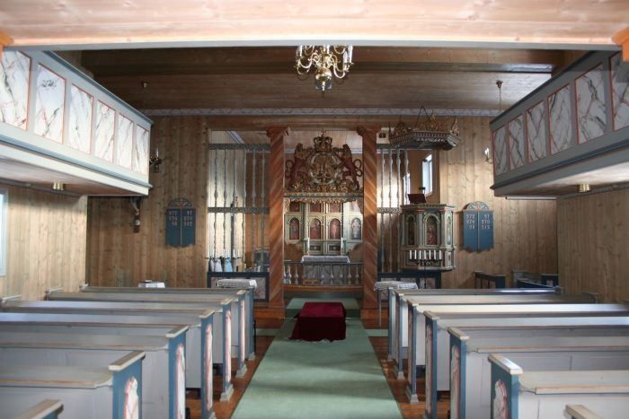 Innvendig trekirke med blå benker på begge sider, grønn midtgang og dekorert altertavle foran..