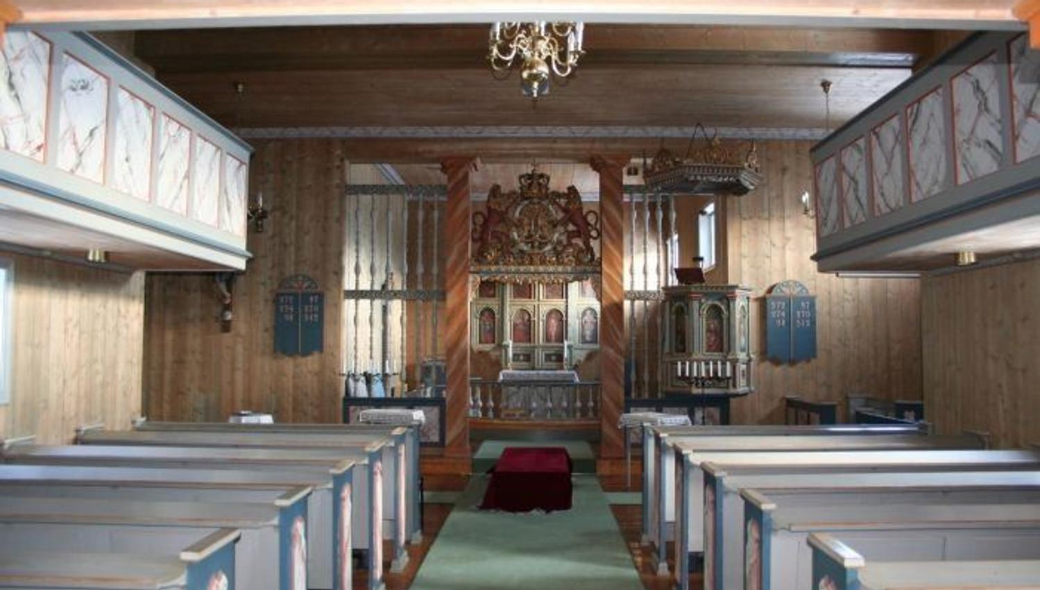 Innvendig trekirke med blå benker på begge sider, grønn midtgang og dekorert altertavle foran..