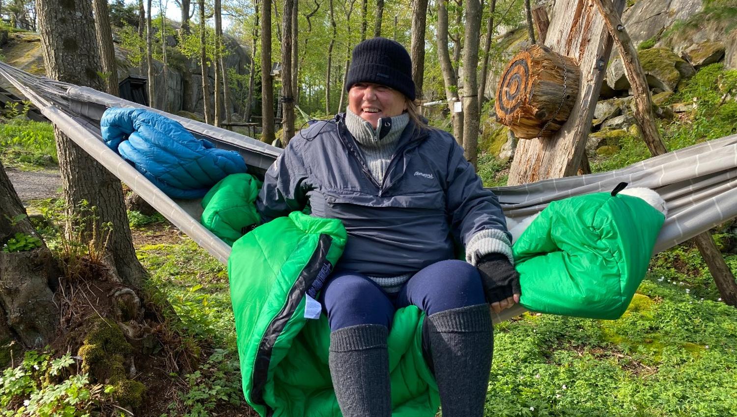 A happy lady has slept in a hammock between the trees. She is well dressed