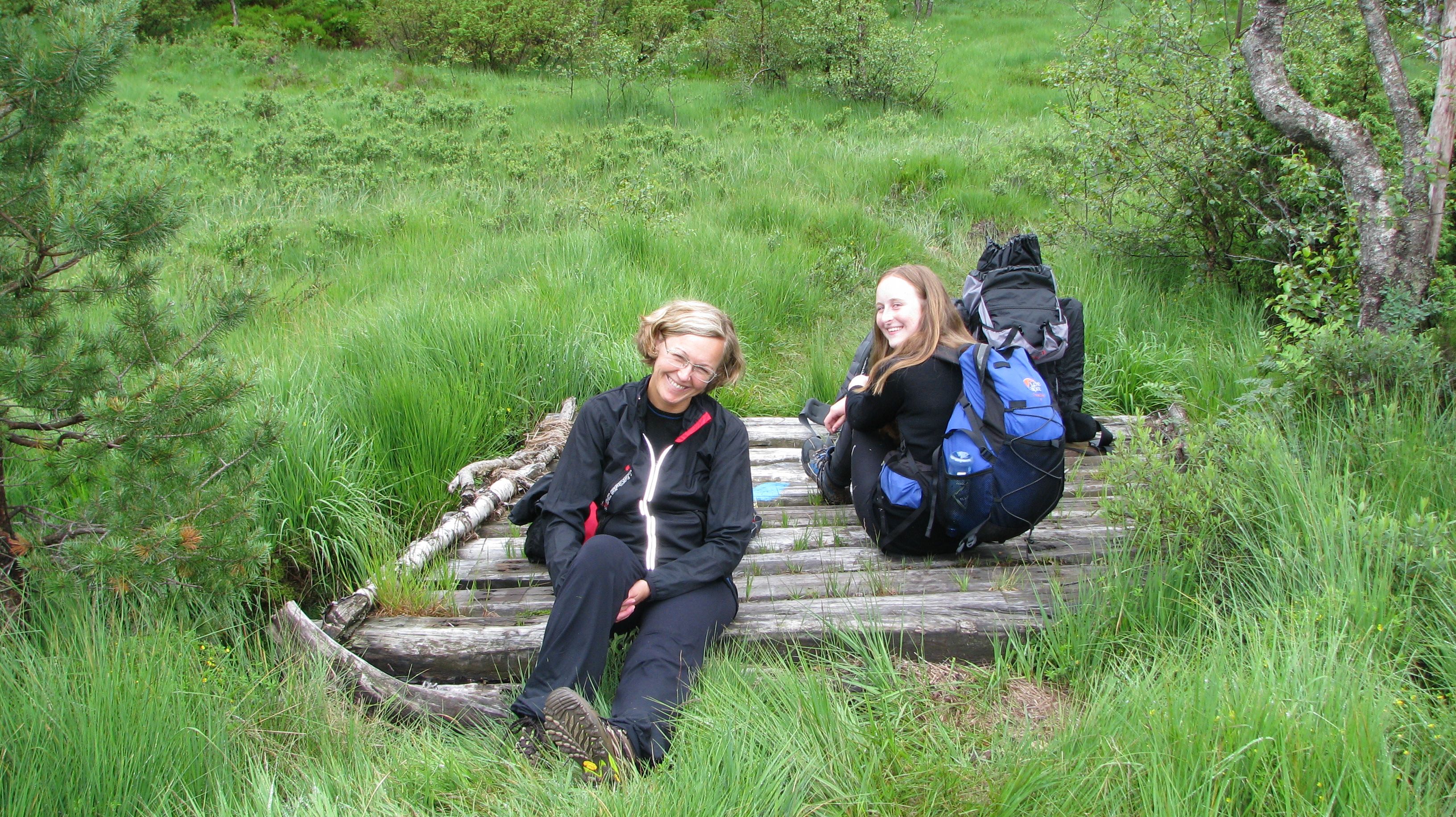 Two smiling women sitting on a small wooden log bridge