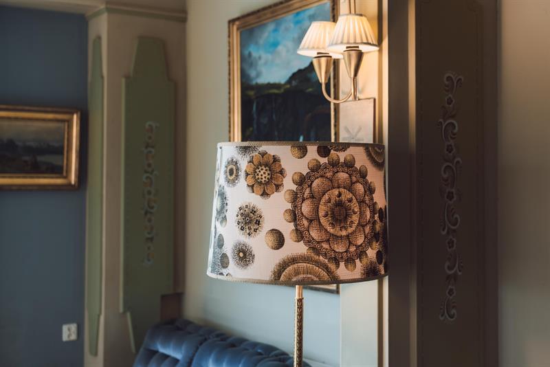An old retro lamp in the foreground with a blue couch and some painitings on the wall in the background.