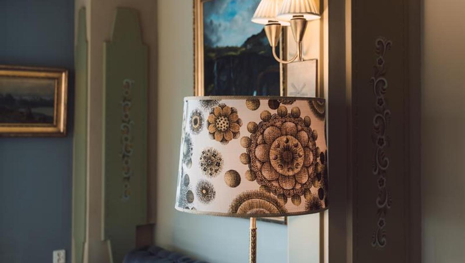 An old retro lamp in the foreground with a blue couch and some painitings on the wall in the background.