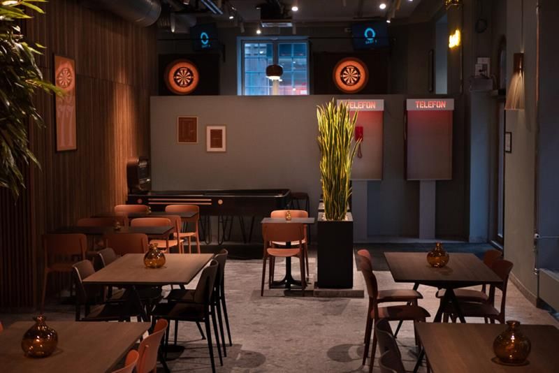 Dark wooden tables and chairs in an elegant room with wood-paneled walls. Two telephone booths and a shuffleboard at the end of the room.