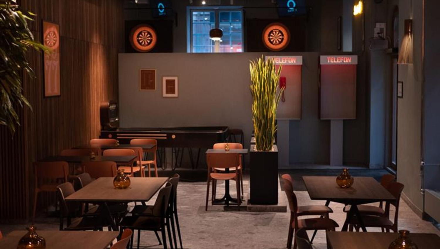 Dark wooden tables and chairs in an elegant room with wood-paneled walls. Two telephone booths and a shuffleboard at the end of the room.