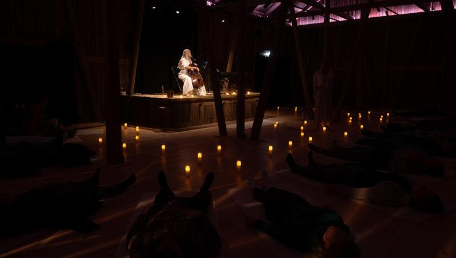 Musiker spiller cello på en scene med varm, dempet belysning og publikum i mørket foran