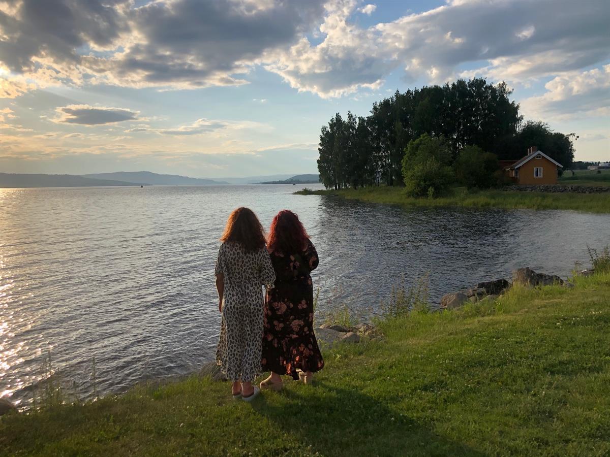 Pilegrimsleden Atlungstad i Stange Vestbygd. To personer står ved vannkanten og ser utover innsjøen ved solnedgang.