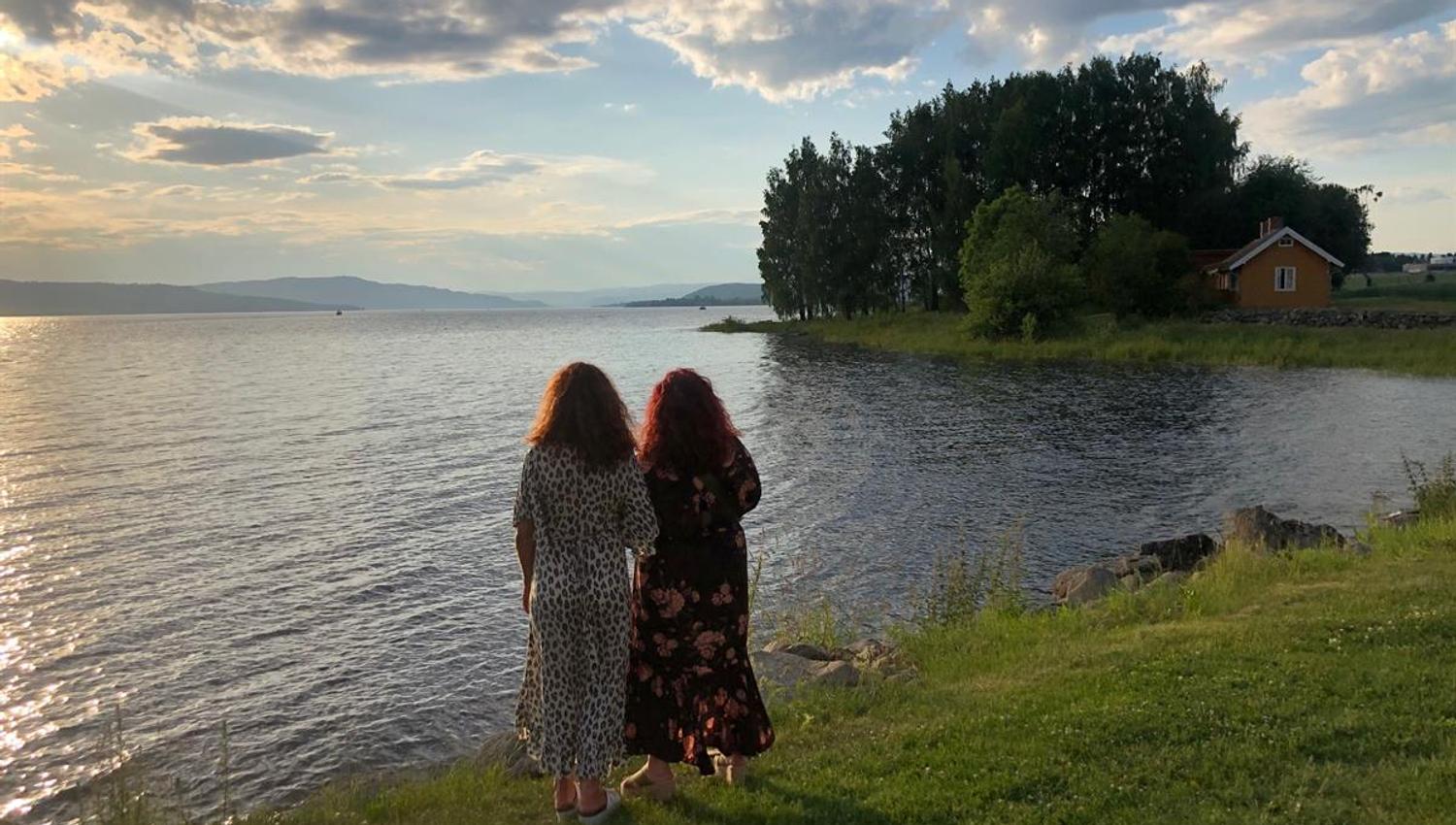 Pilegrimsleden Atlungstad i Stange Vestbygd. To personer står ved vannkanten og ser utover innsjøen ved solnedgang.