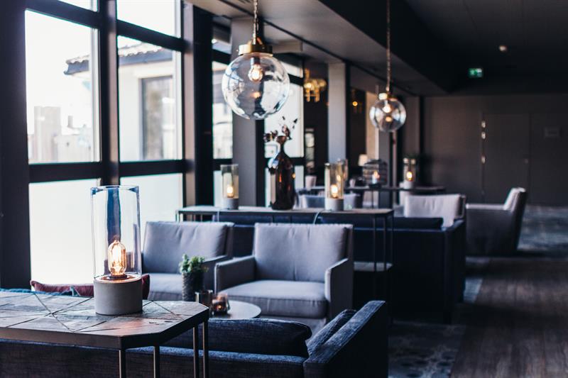 Photo from inside the restaurant. Gray sofa and two chairs with large round lamps above the tables.