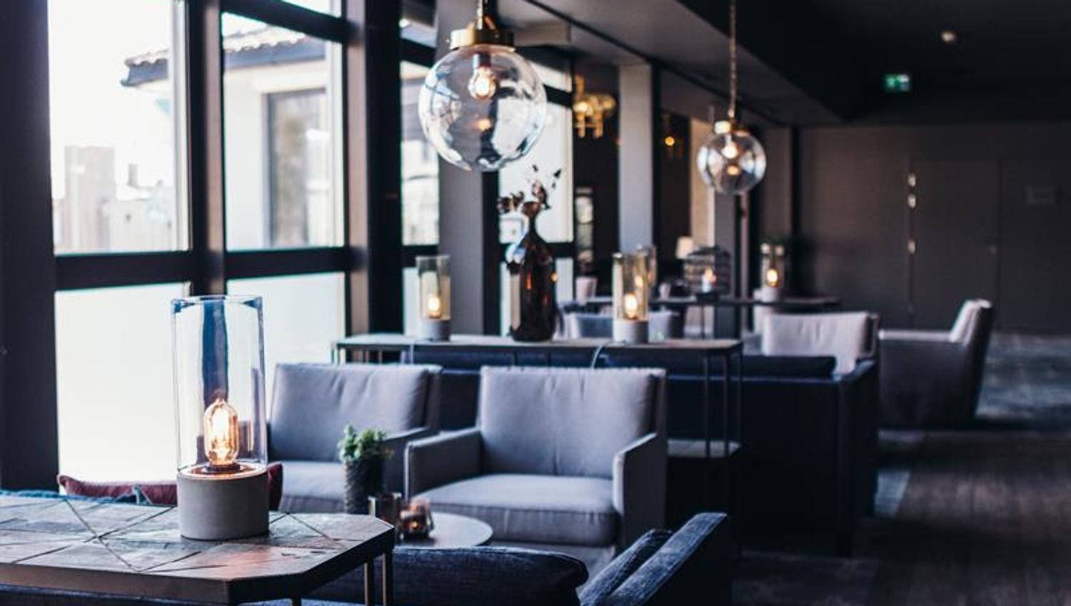 Photo from inside the restaurant. Gray sofa and two chairs with large round lamps above the tables.
