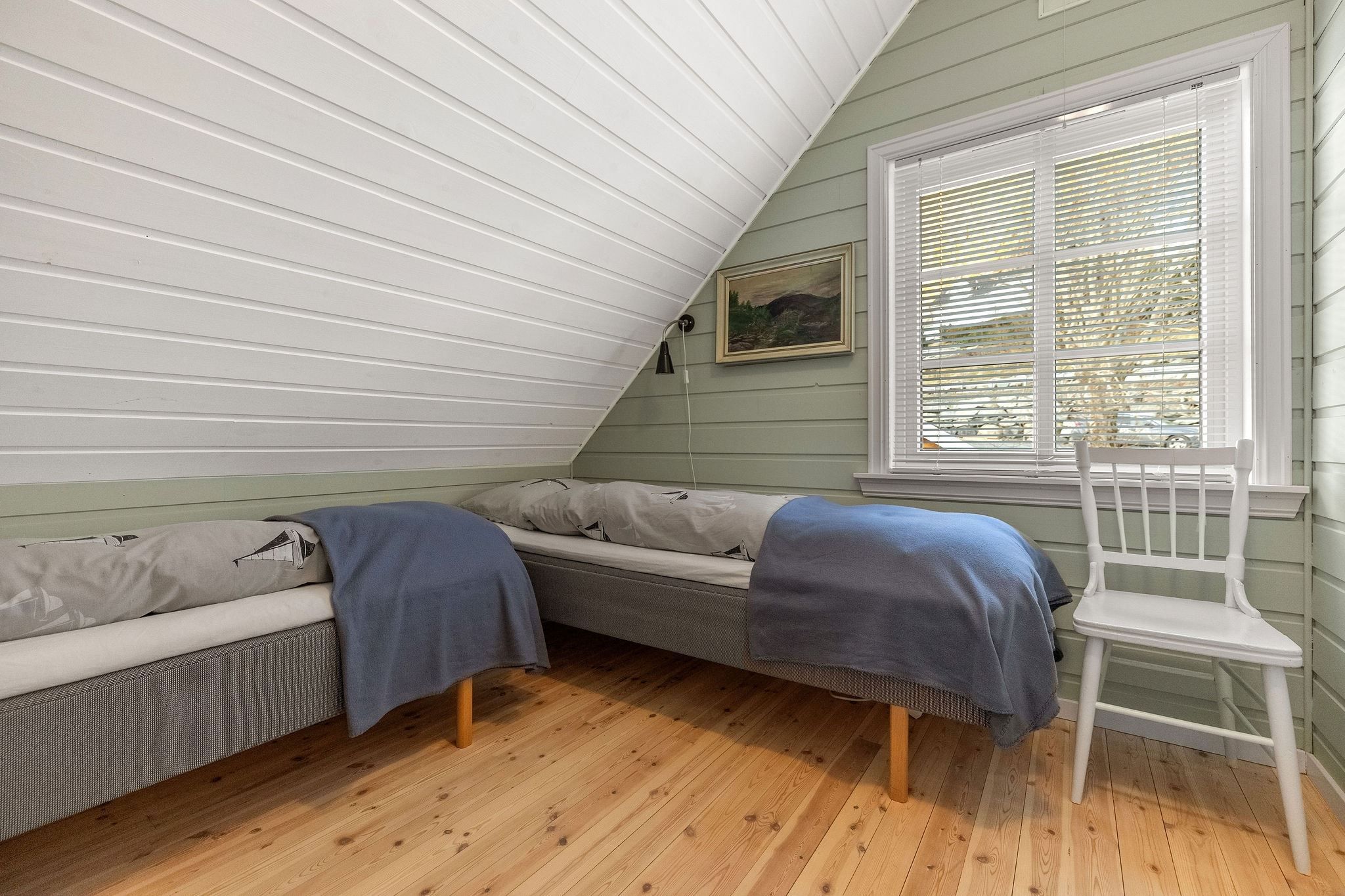 Small attic bedroom with two single beds, blue blankets, wood floor, window blinds, and a white chair at the Seahouse at Hornelen Panorama in Bremanger..