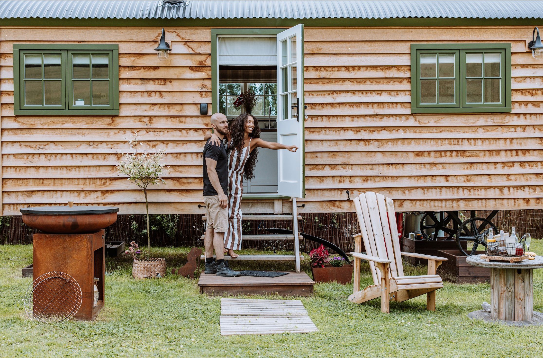 couple going into a Small wooden house with green windows and chairs in front 