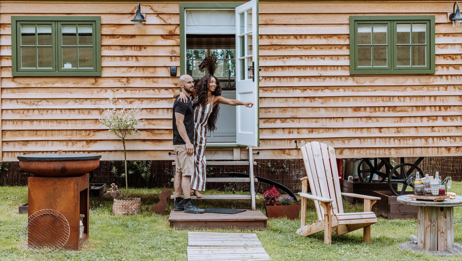 couple going into a Small wooden house with green windows and chairs in front