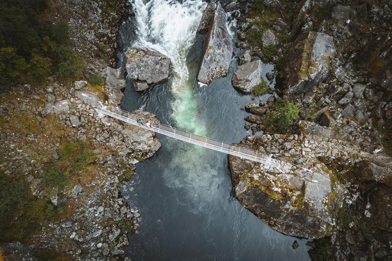 A top-down droneshot of people walking across the new bridge below the waterfall.