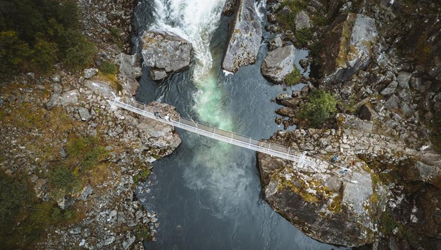 A top-down droneshot of people walking across the new bridge below the waterfall.