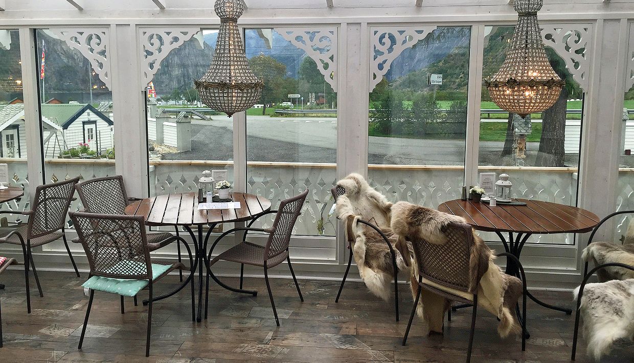 A dining terrace with tables and chairs, sheep skins in some chairs and chandelairs hanging from the ceiling.