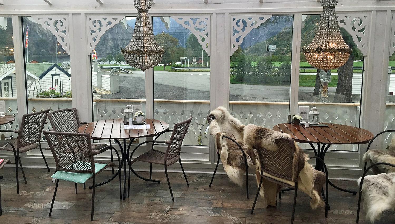 A dining terrace with tables and chairs, sheep skins in some chairs and chandelairs hanging from the ceiling.