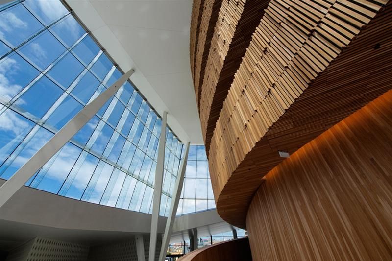 Interior photo of a brown, wooden set of stairs opposite a big glass windows towards the blue sky.