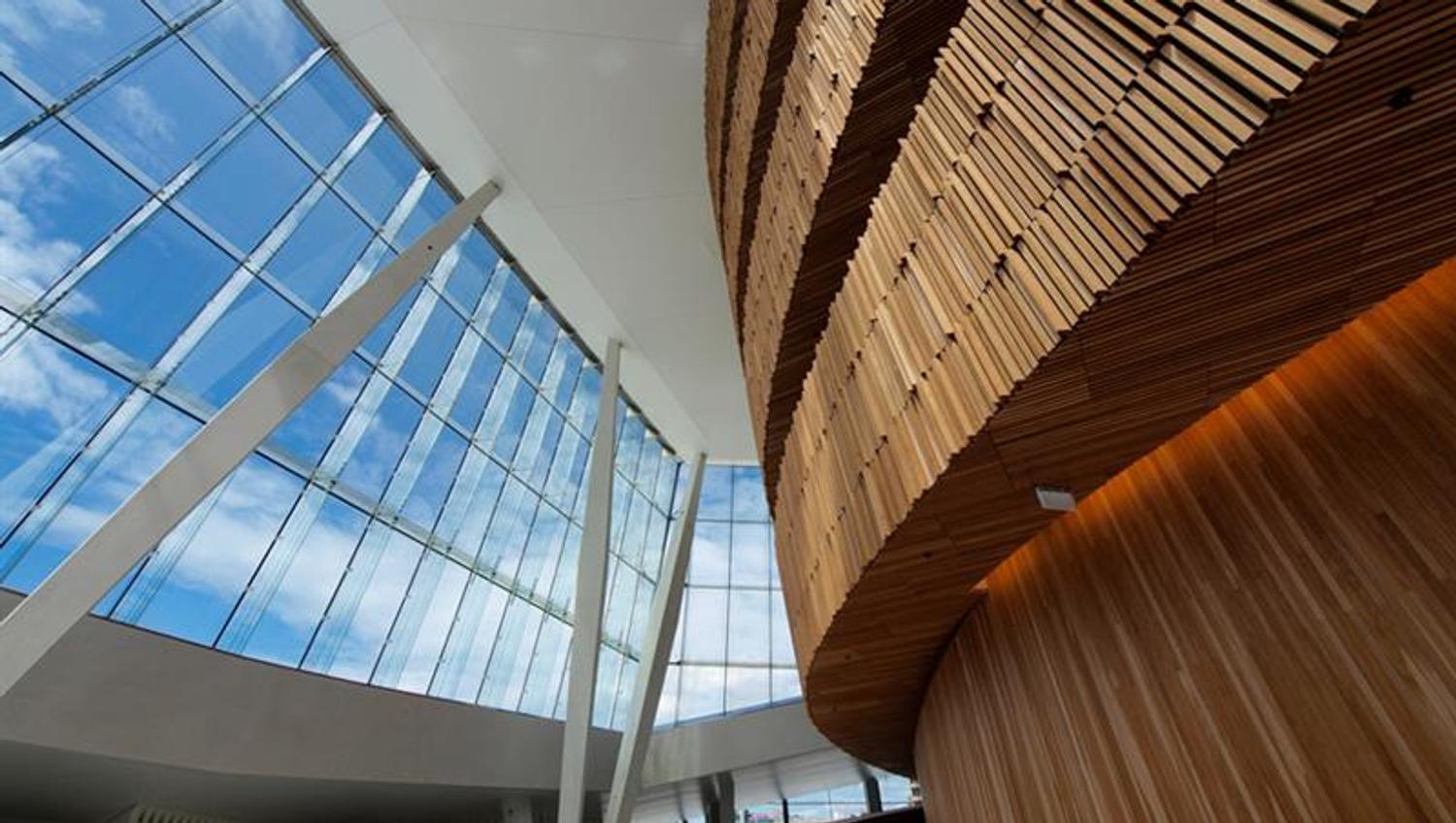 Interior photo of a brown, wooden set of stairs opposite a big glass windows towards the blue sky.