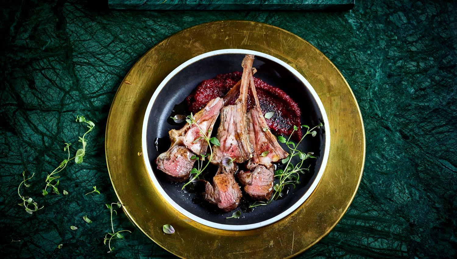 Overhead view of lammecarre on a black plate with red beet sauce and microgreens on a green surface at Sølvane Farm Hotel Restaurant in Kandal, Gloppen..