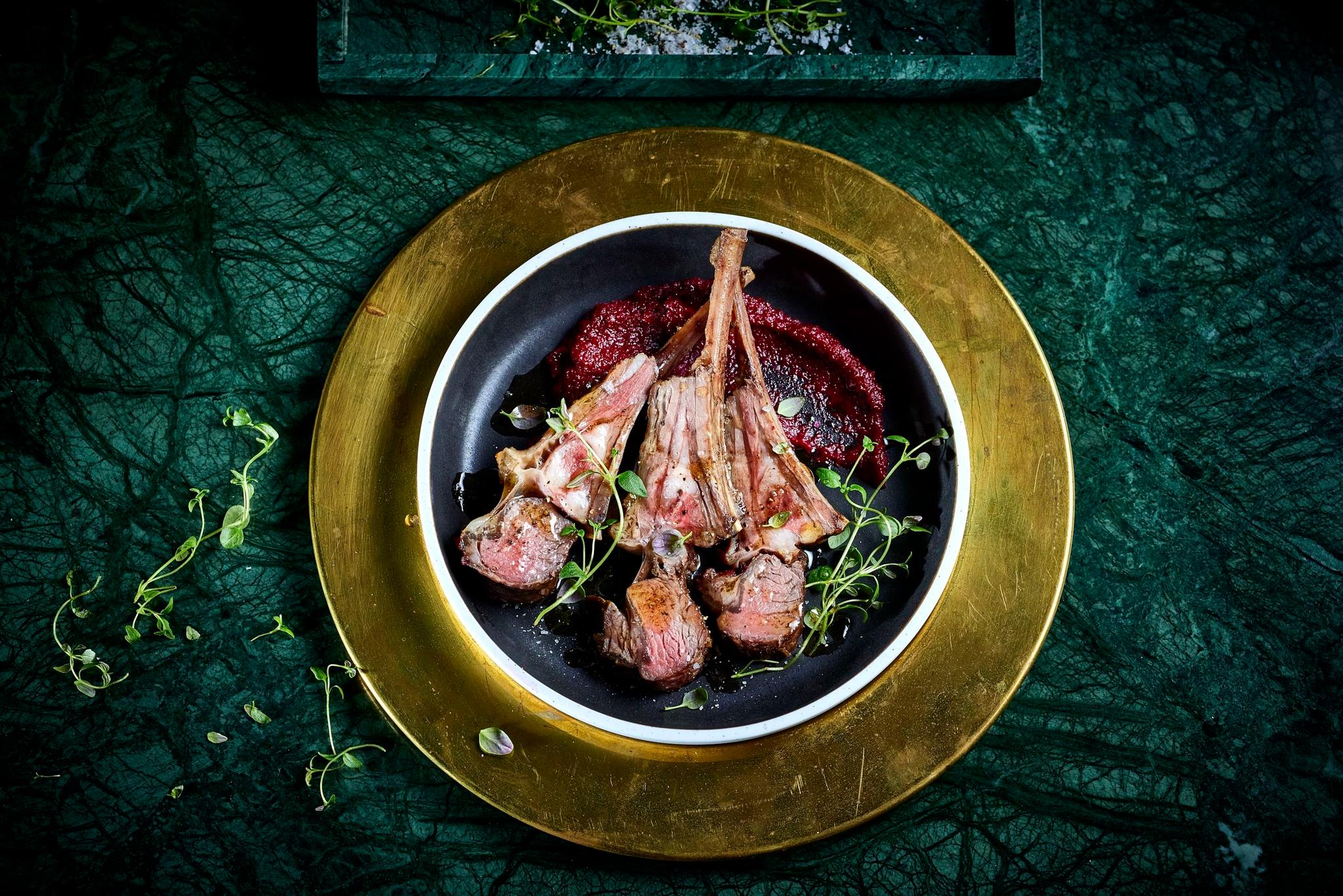 Overhead view of lammecarre on a black plate with red beet sauce and microgreens on a green surface at Sølvane Farm Hotel Restaurant in Kandal, Gloppen..