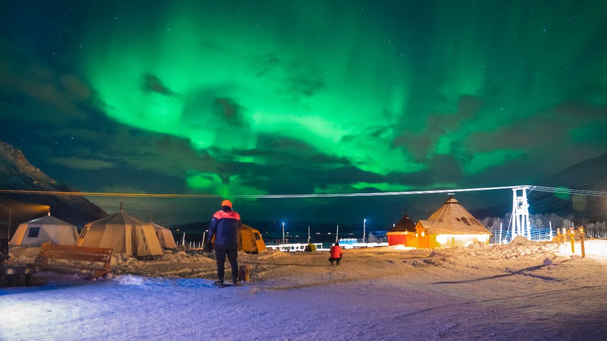 Bright Northern Lights above Tromsø Lapland’s reindeer camp and lavvus in a snowy landscape.