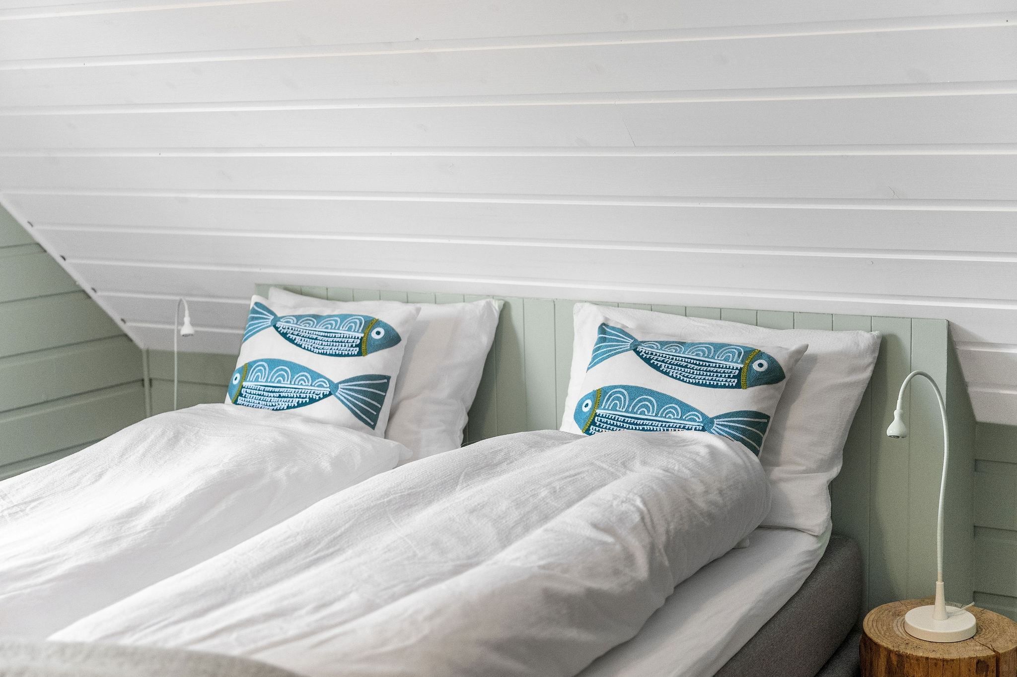 Two neatly made twin beds with white bedding and blue fish-pattern pillows under a slanted white wood ceiling at the Seahouse at Hornelen Panorama in Bremanger..