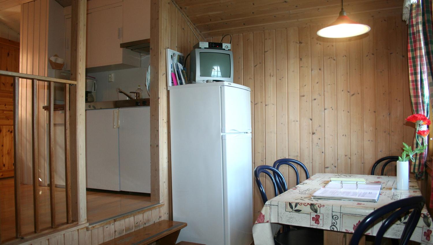 Traditional cabin kitchen with dining table and TV in an older cabin at Oddland Camping.