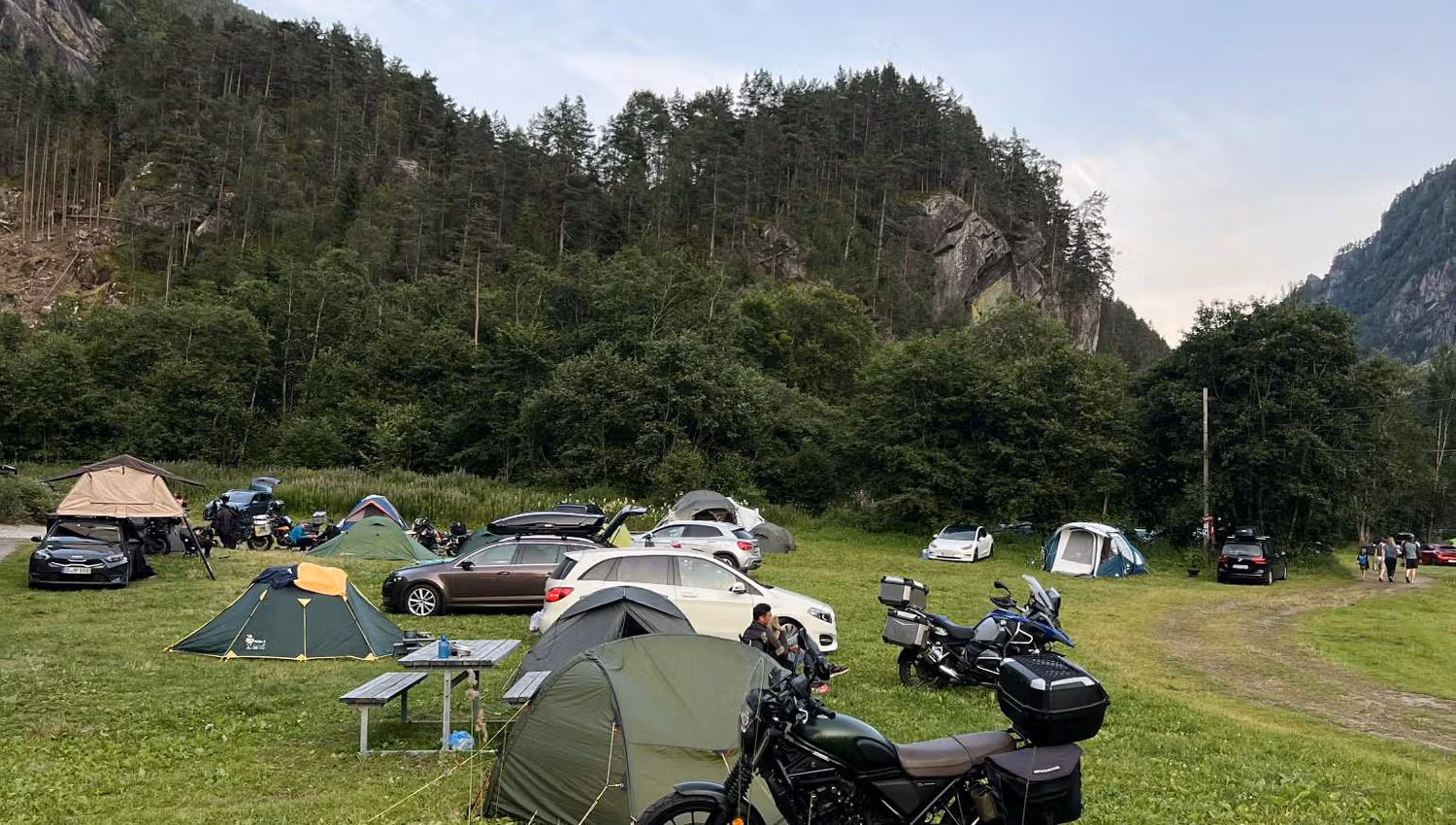 Motorräder und Zelte auf dem Hildal Camping, umgeben von grünen Bergen an einem Sommerabend.