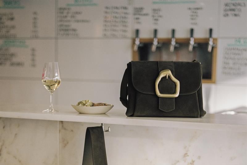 A bag next to a glass of white wine.