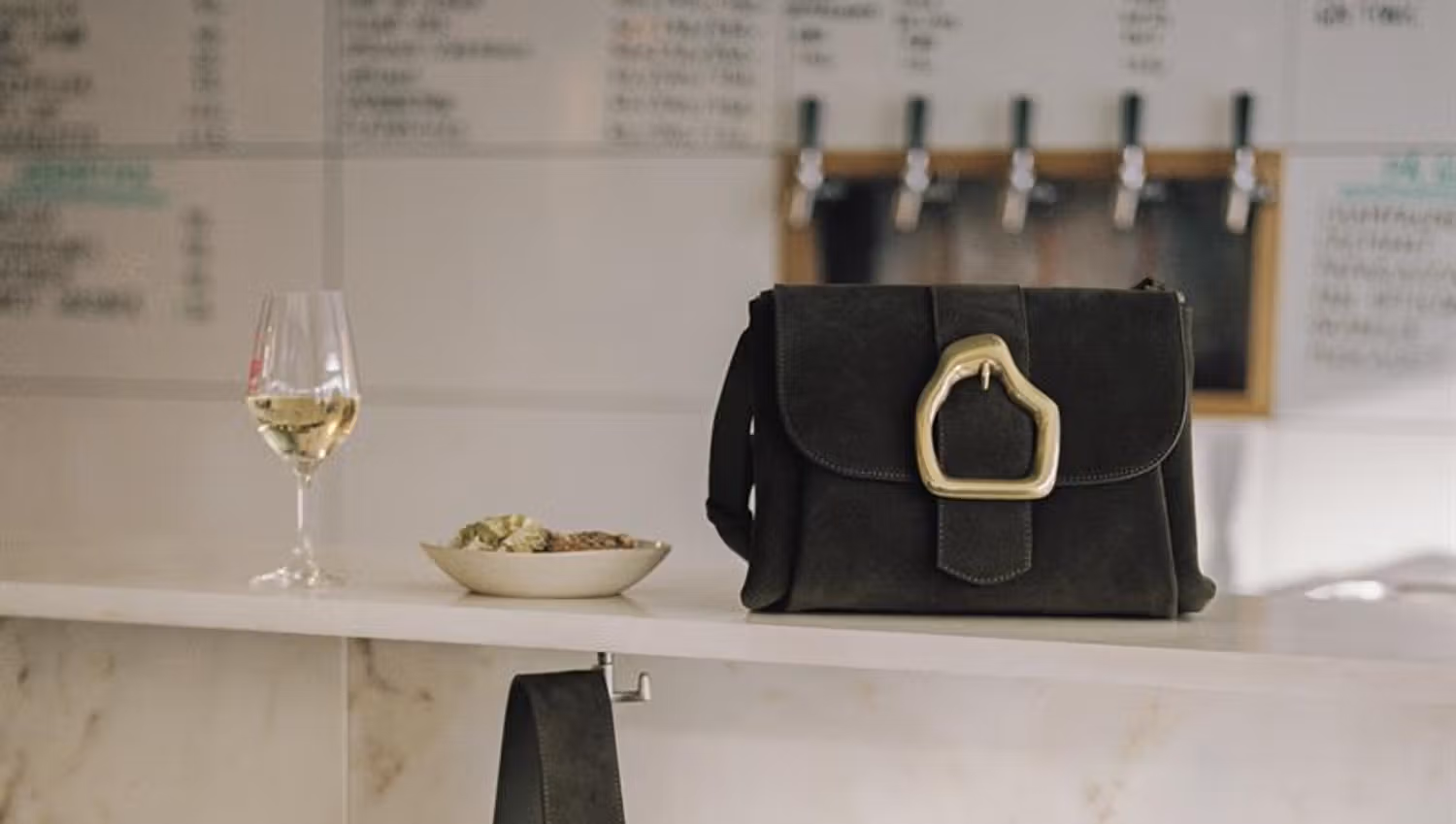 A bag next to a glass of white wine.