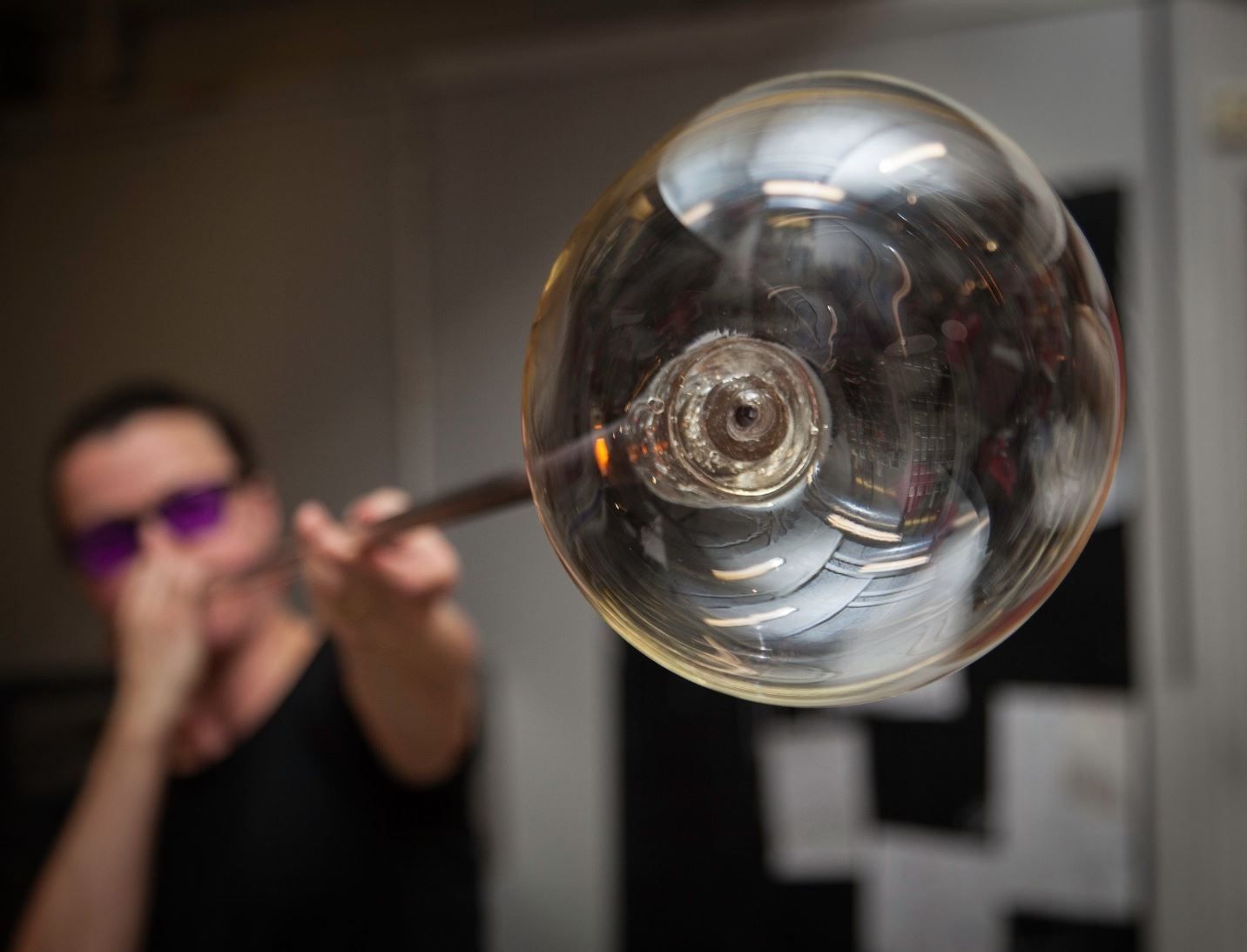 A spherical glass artwork in the foreground, with a glassblower working in the background at Blåst Glass Studio in Tromsø.