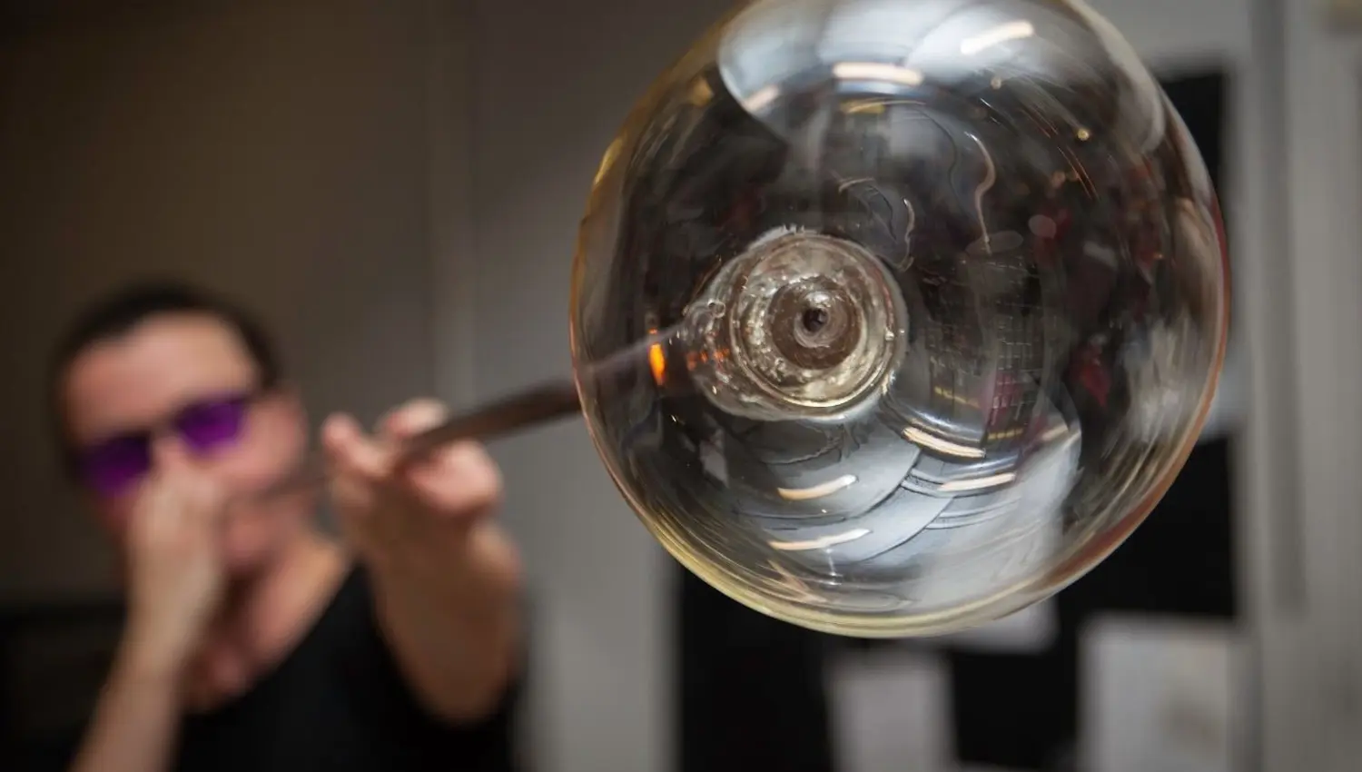 A spherical glass artwork in the foreground, with a glassblower working in the background at Blåst Glass Studio in Tromsø.