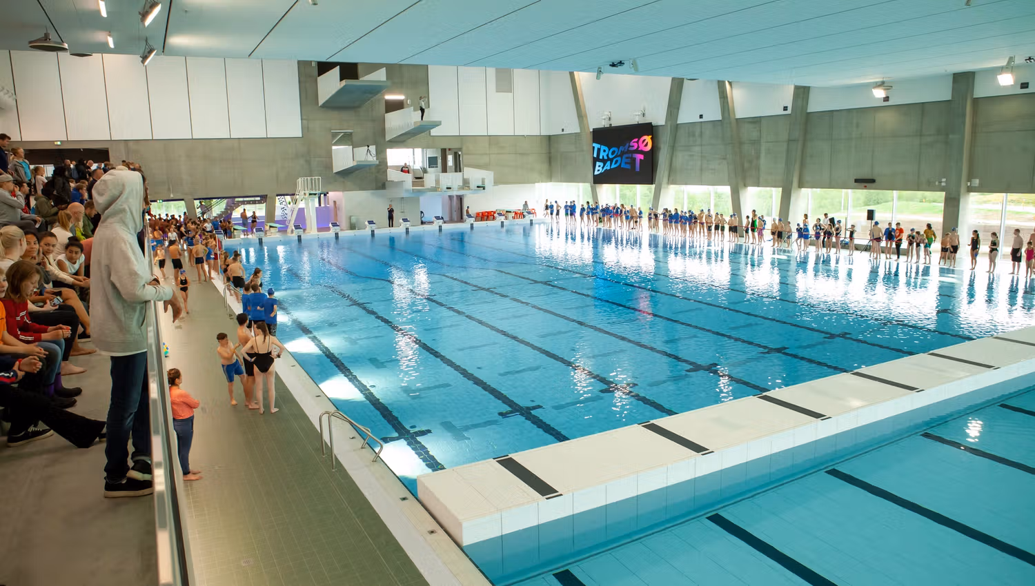 Indoor swimming pool with spectators and the sign TROMSØ BADET on the wall