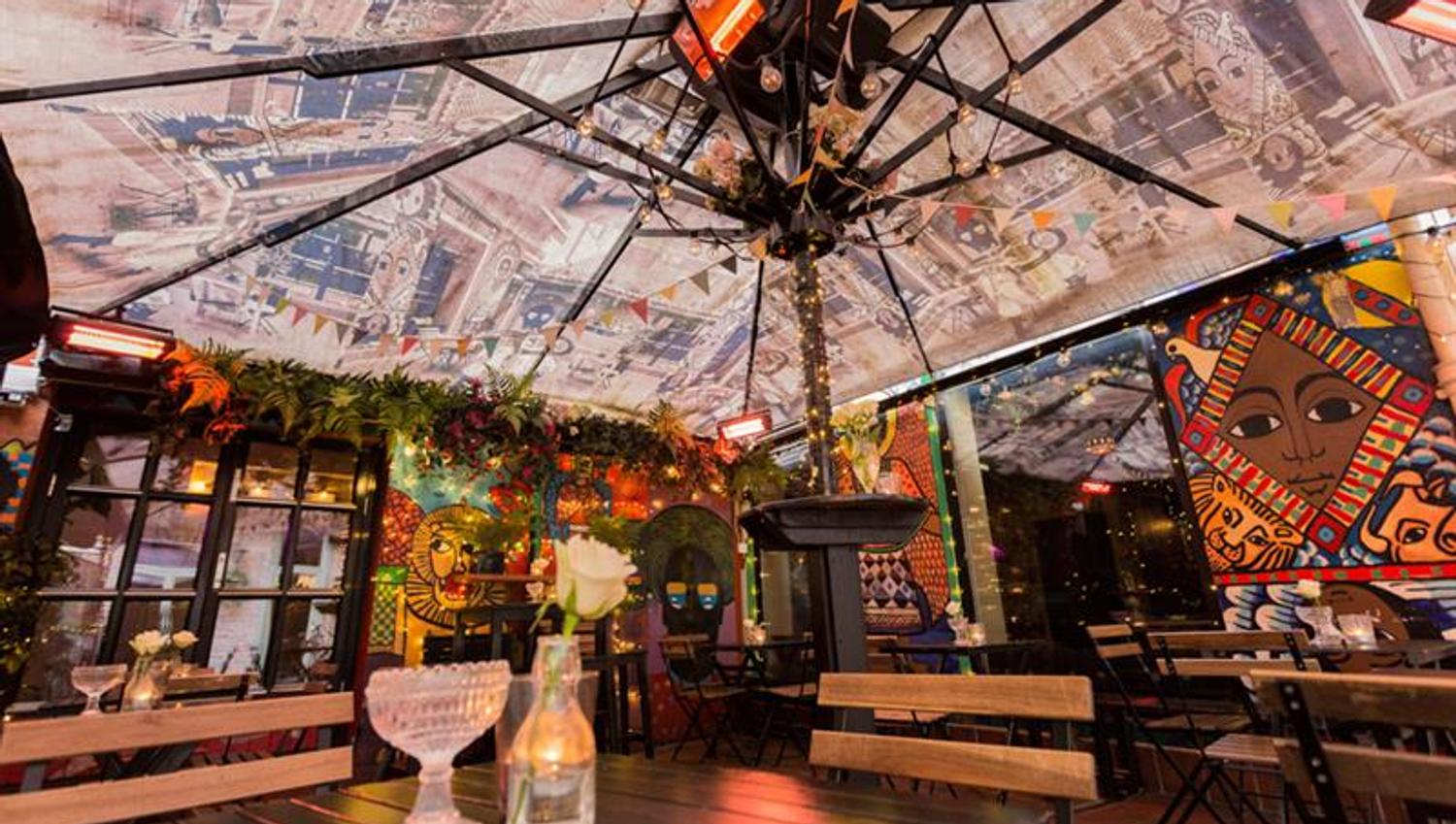 Outdoor seating, table and chairs under a parasol. A glass and a vase with a flower on the table.