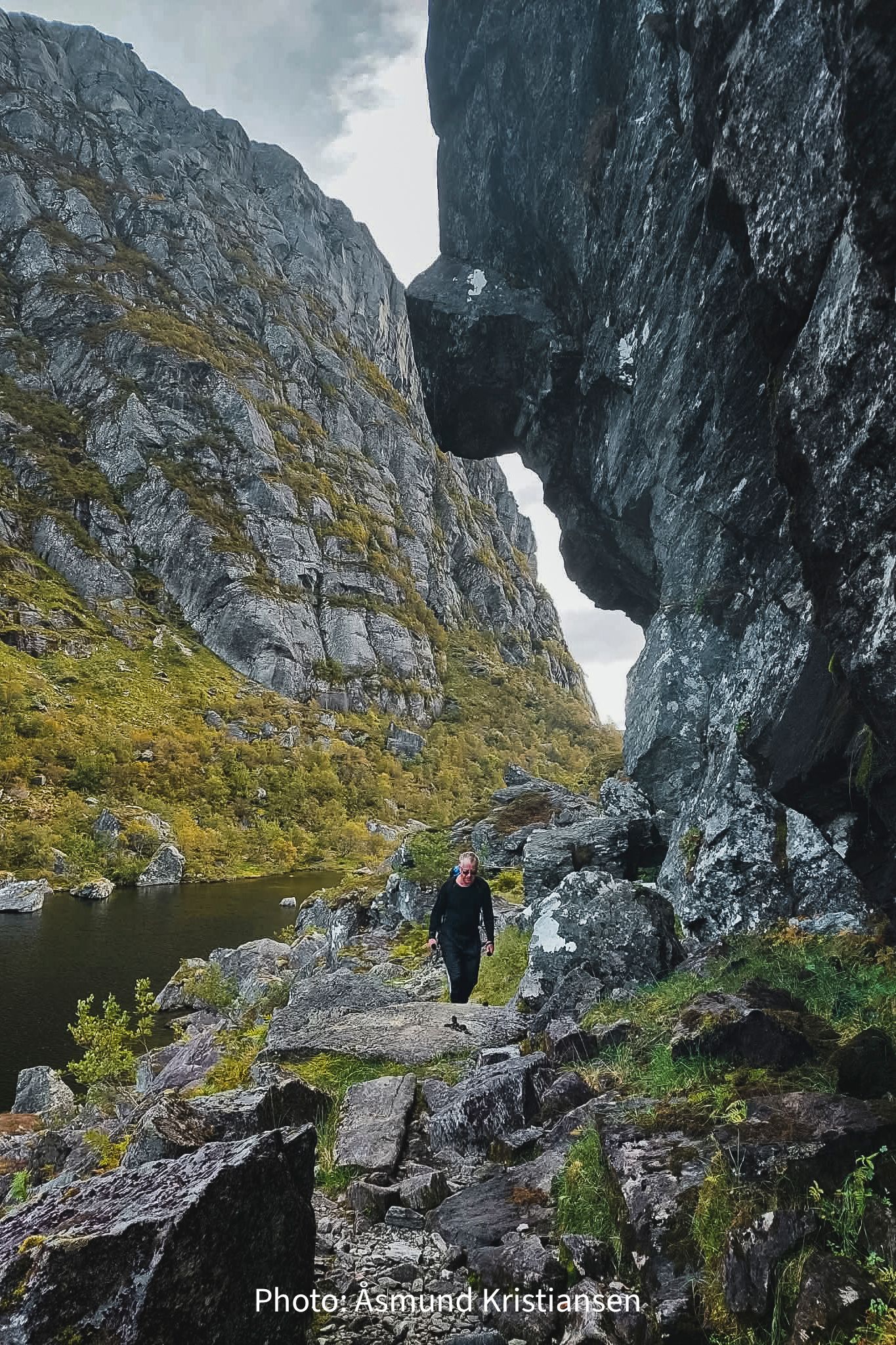 Hiker walking through a narrow mountain valley in Hardanger, Norway, with water and dramatic rock formations
