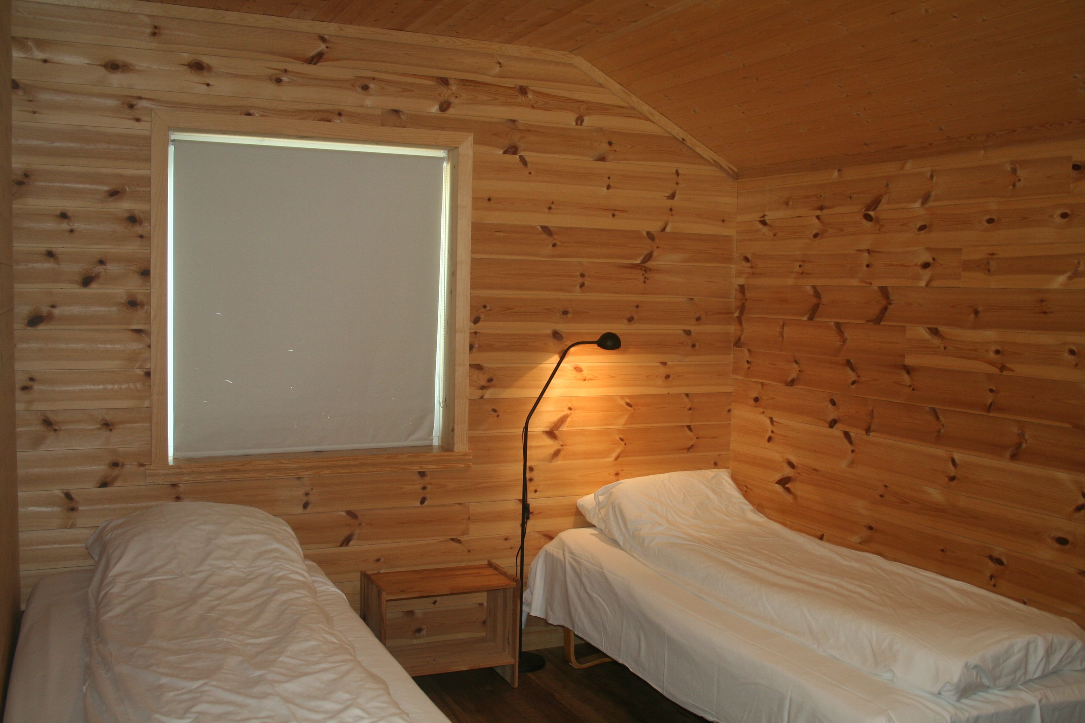 Bedroom with natural wood paneling and two single beds at Vågen Rooms and Cabins.