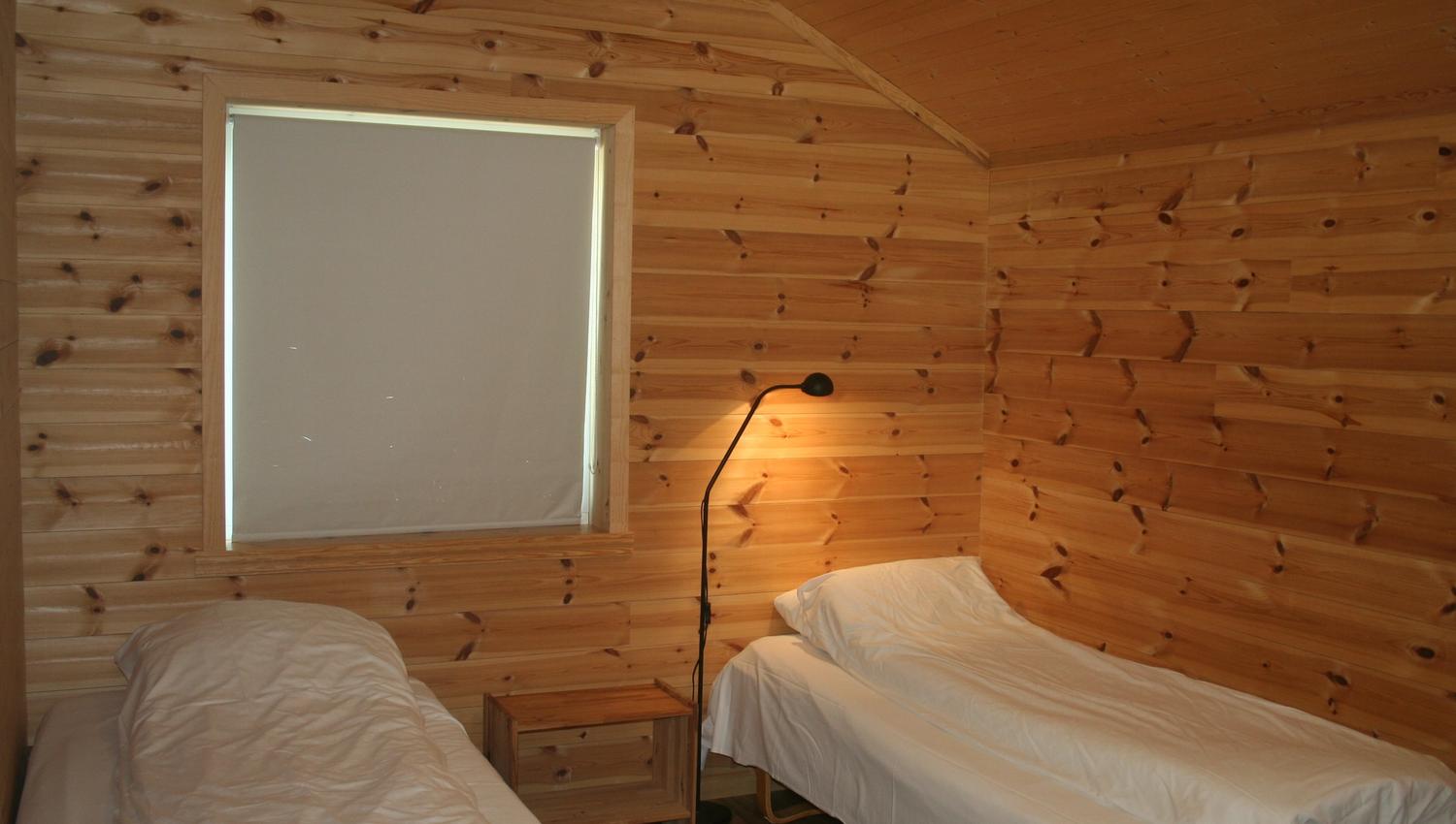 Bedroom with natural wood paneling and two single beds at Vågen Rooms and Cabins.